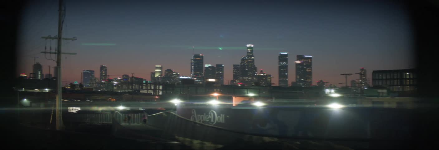 Vehicle passes people moving along a path at night with the city skyline in the background