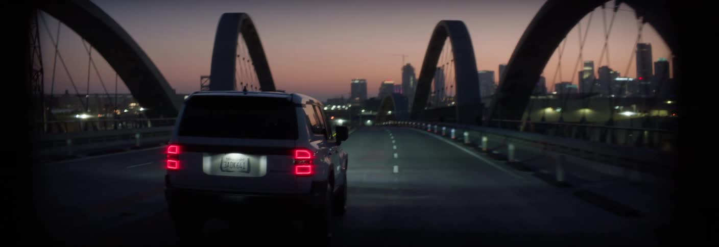 White car driving over an overpass with a skyscraper of a metropolis on the horizon
