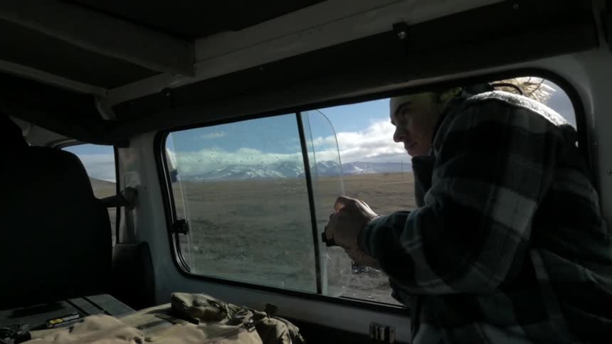 Man hanging out the window of a moving vehicle on a sunny day