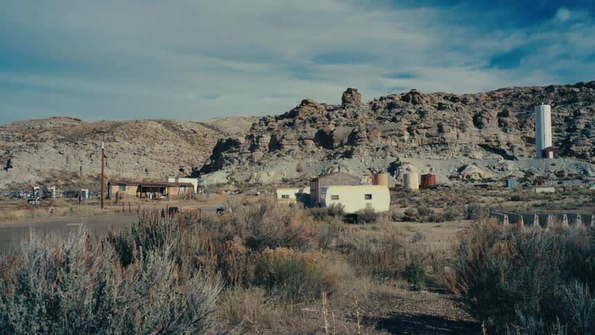 Houses in a desert area with sparse vegetation and canyons in the background