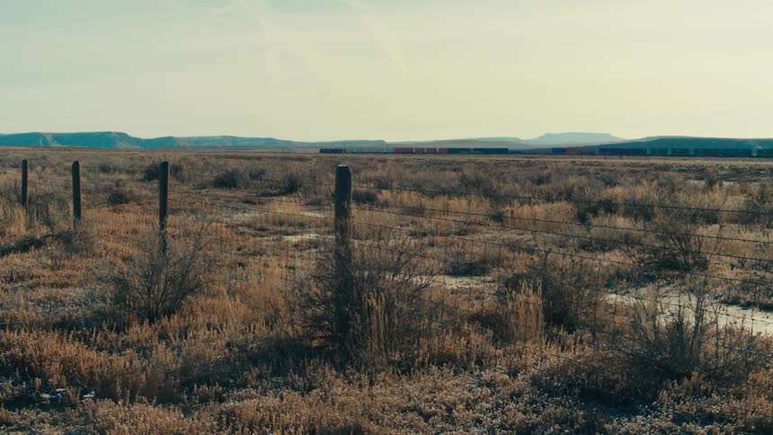 A long freight train chugs across a vast open landscape dwarfed by the vast expanse of the horizon