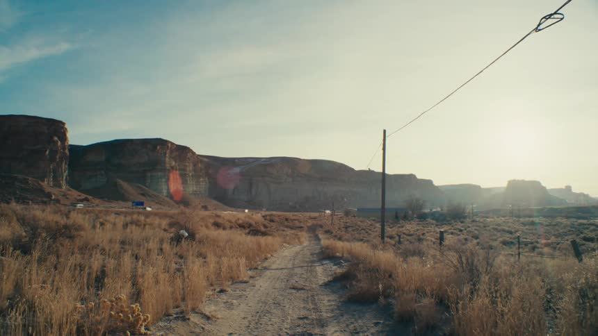 A dirt road winds through a desolate landscape leading towards a distant cliff face under a hazy sky