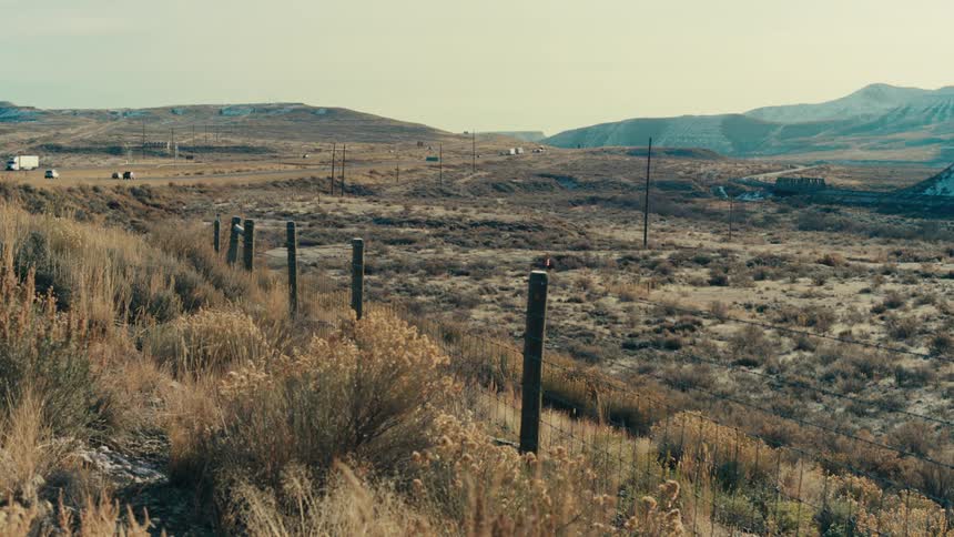Landscape of a terrain with sparse vegetation and mountains and in the background a highway with vehicle traffic