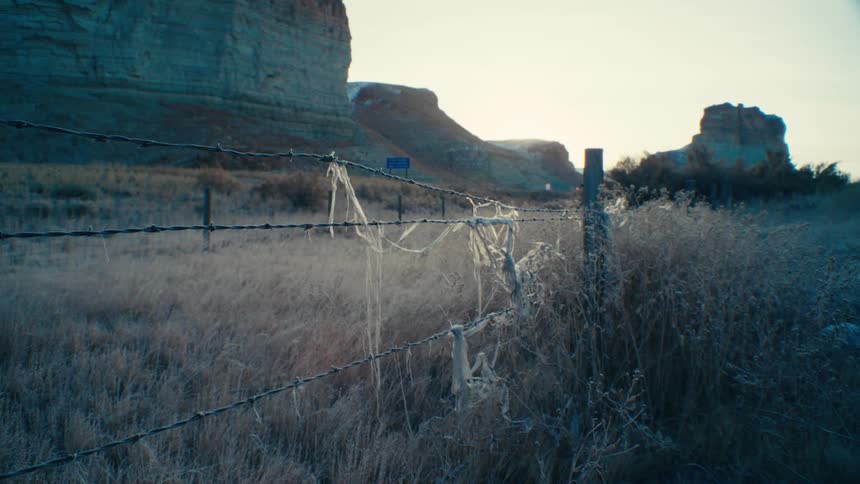 Barbed wire fence in the foreground and in the background a highway next to canyons