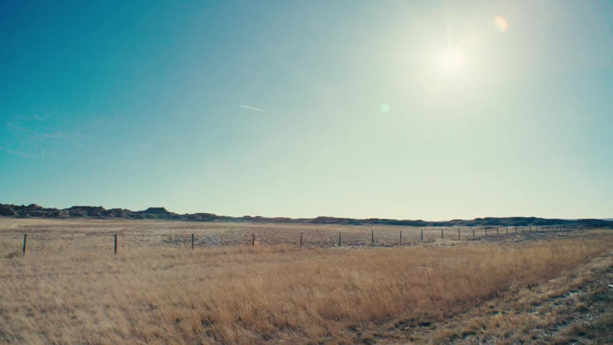 A vast open landscape with a fence stretching across the horizon under a bright blue sky with the sun shining brightly