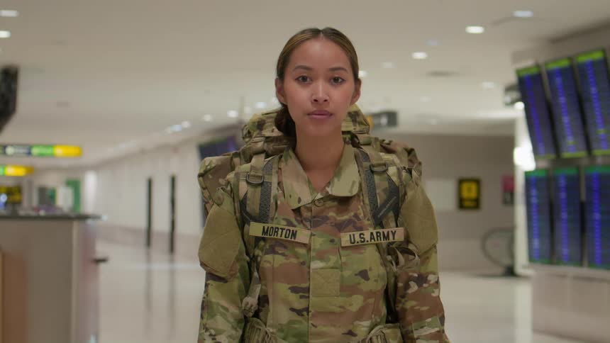 A female soldier in us army fatigues and a backpack stands in an airport terminal