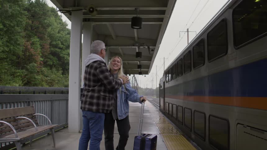 Father and daughter hug before she moves towards boarding the newly arrived train during a misty day