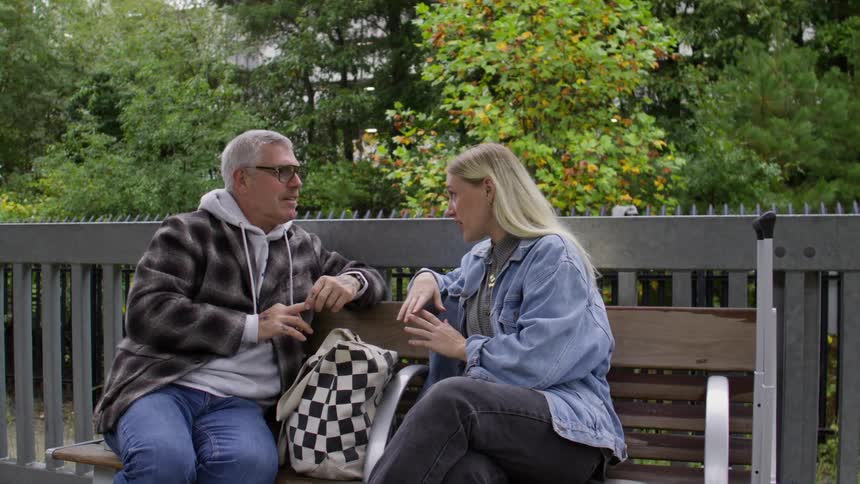 Woman and a man sitting on a wooden bench in an outdoor terminal