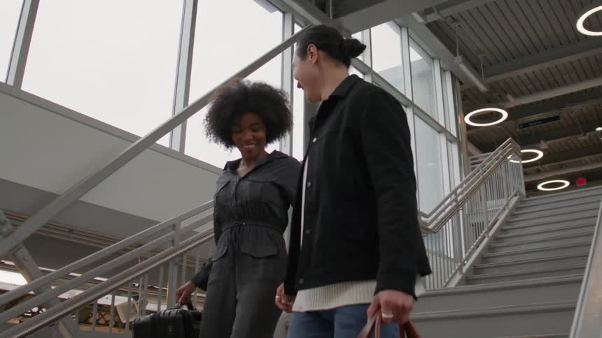 Couple holding hands holding backpacks and walking down the stairs of a terminal