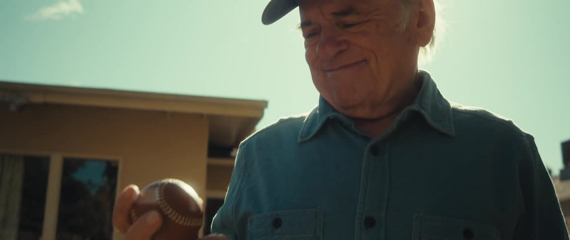 Cheerful elderly man in a backyard holding a baseball