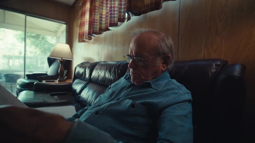 Elderly man sitting on a leather sofa reading a document