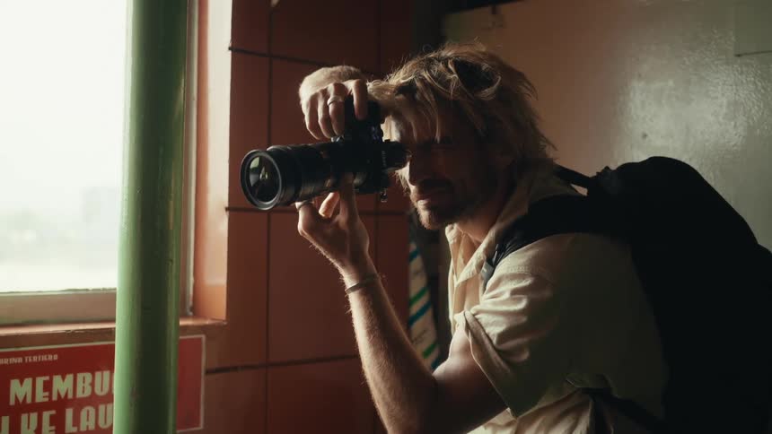 A blonde man with long hair gives instructions to a model while taking pictures