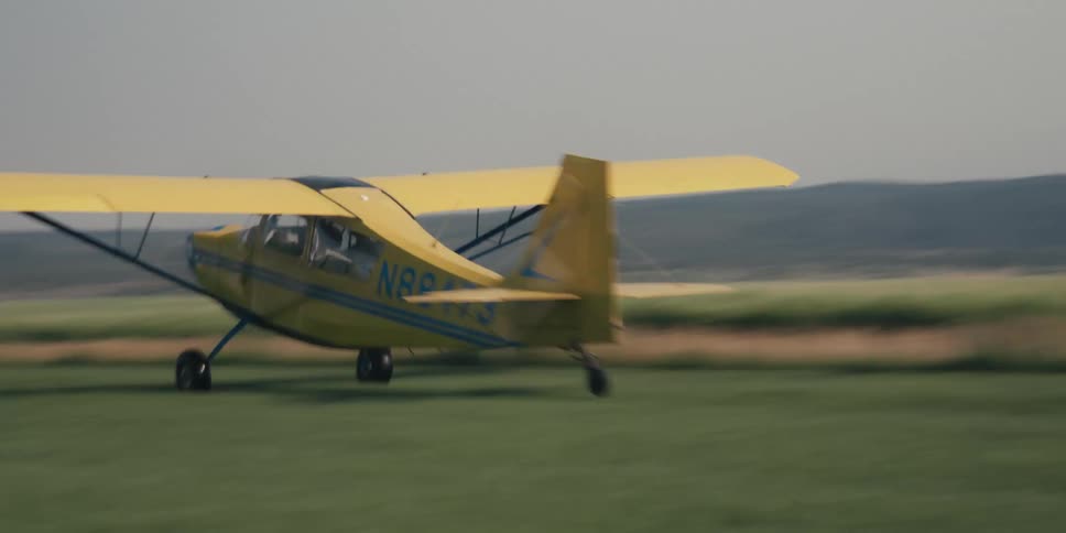 A small propellerdriven airplane taxis along a grassy runway ready for takeoff against a hazy sky