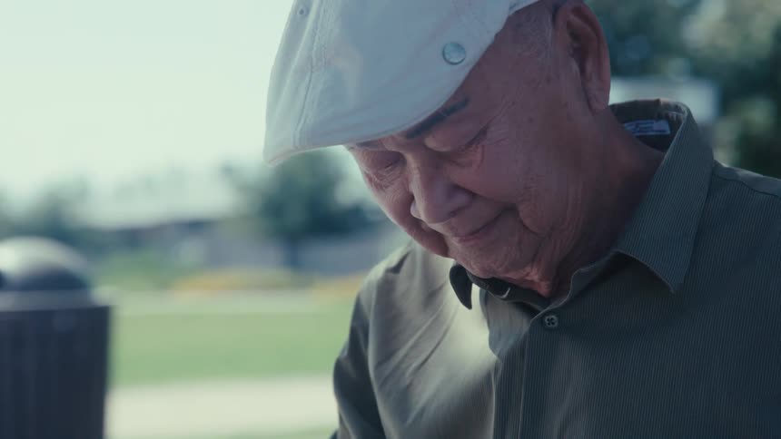 Elderly man looking down while standing in an outdoor setting