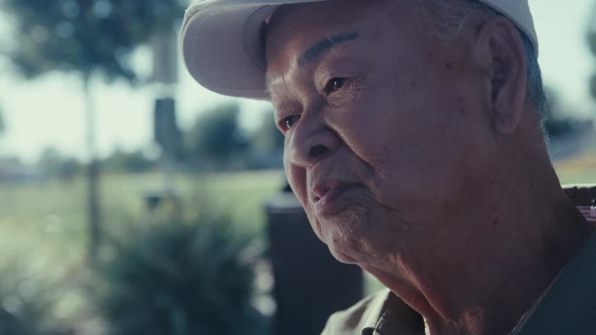 Close up of an elderly man sitting in a park talking on a sunny day