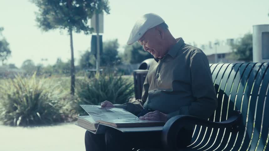 Man sitting outside on a bench smiling as he looks at a photo album