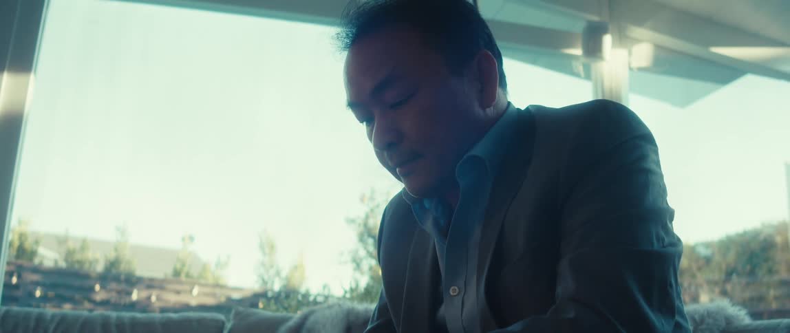 A man wearing a business suit uses a smartphone in front of a laptop at home