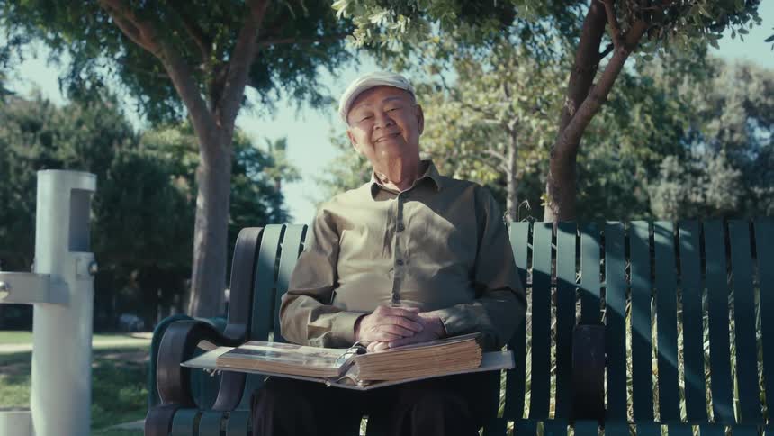 Man sitting alone on a park bench and waving to the camera