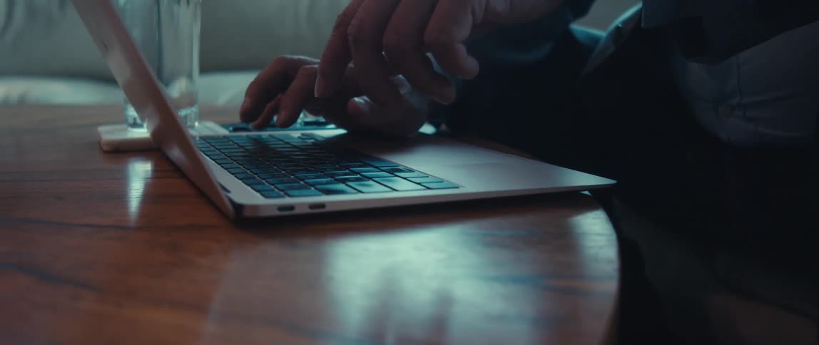 A mans hands are typing on a laptop keyboard illuminated by the glow of the screen