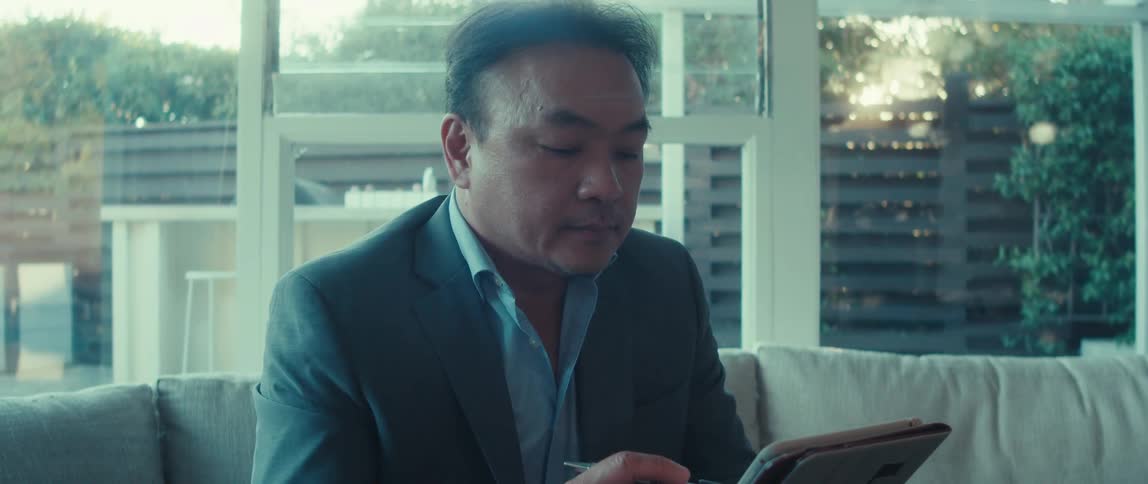 A man in a suit is sitting and typing on a tablet using a stylus