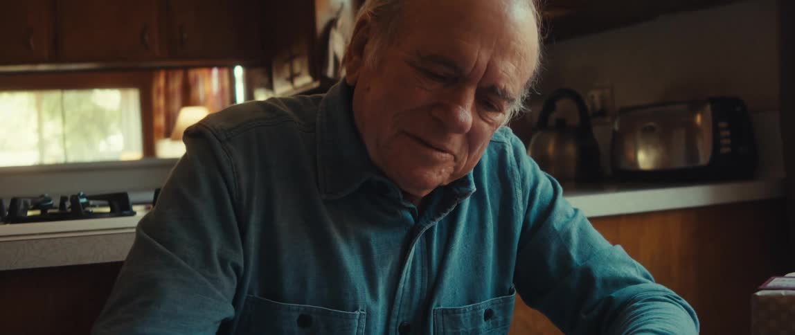 An elderly man writing a note in the kitchen table at home