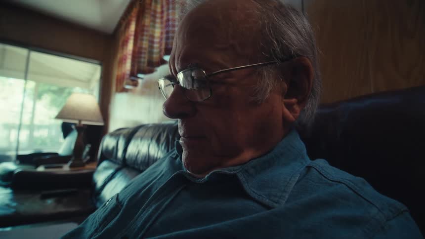 An elderly man reading documents while sitting on a couch at home
