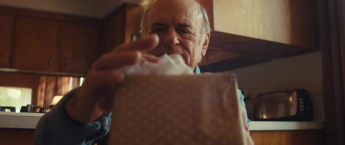 A man puts a ribbon on a gift while smiling