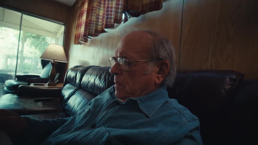 An elderly man sitting on a couch at home reading documents
