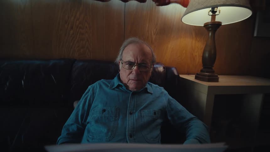 An elderly man sitting in a couch at home reading documents