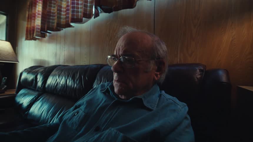 An elderly man sitting on a couch at home reading documents