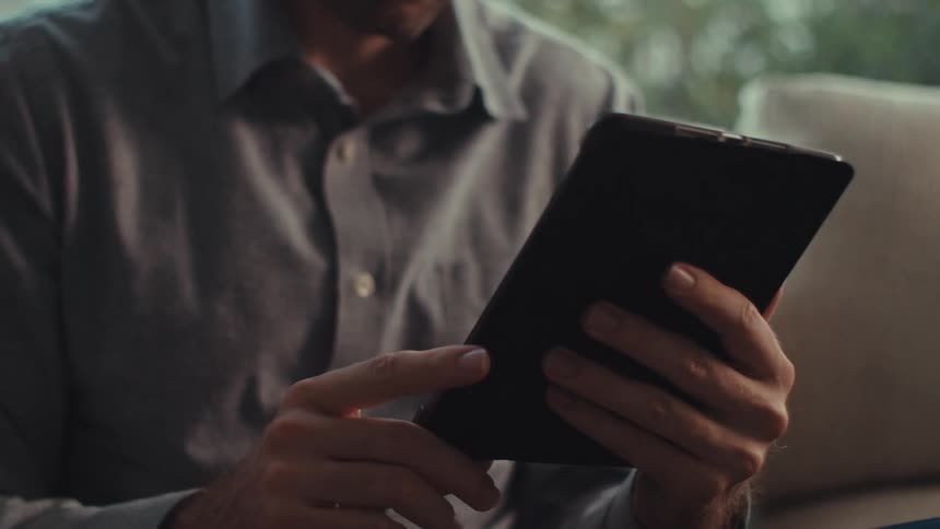 A man wearing a gray shirt holding and interacting with a tablet device