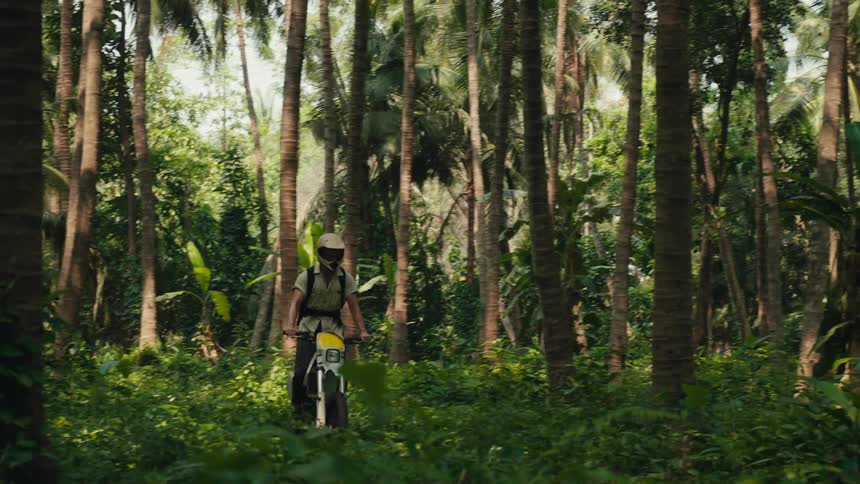 A person wearing a helmet riding a motorcycle in a forest and he is standing on the motorcycle