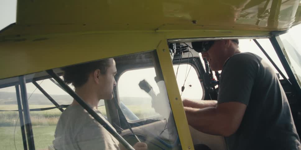 A person sitting in a small singleengine plane and another person putting headphones on their head