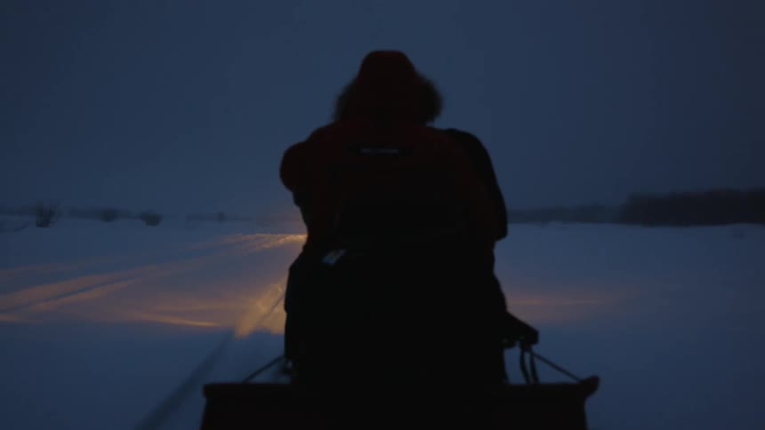 A man is riding his snowmobile through the snow