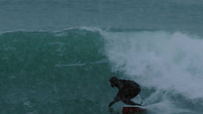 A man surfing a wave during a light snowstorm wipes out
