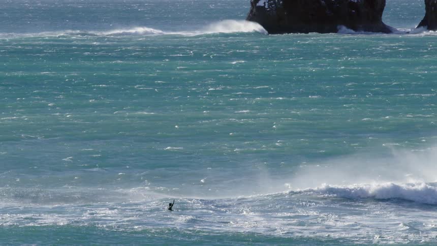 A person is floating on turquoise waves near a rocky outcrop in the ocean