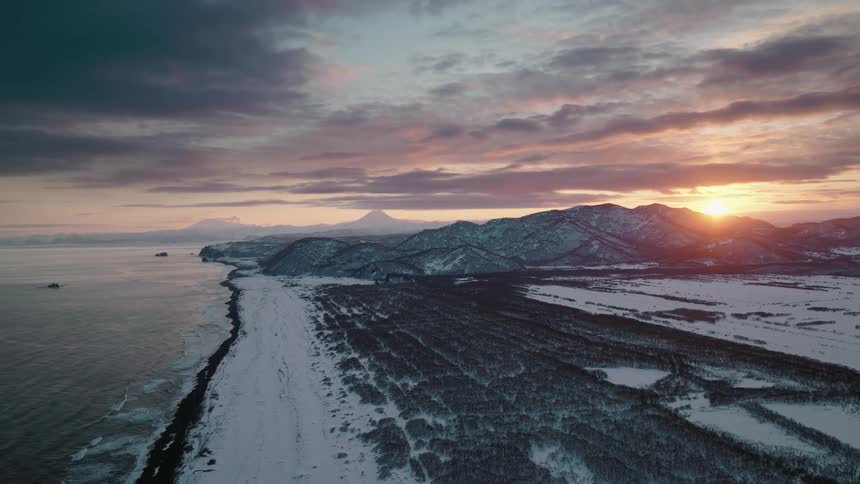 The sun is setting in the horizon of the snow covered mountains