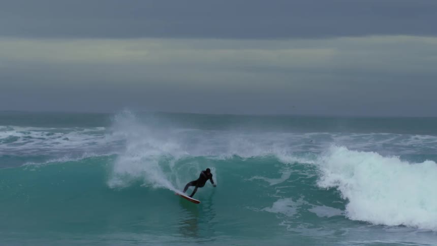 Person is riding waves with their surfboard at dusk