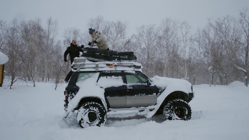Men removing straps holding a snow tube to the roof of a car as snow comes down around them