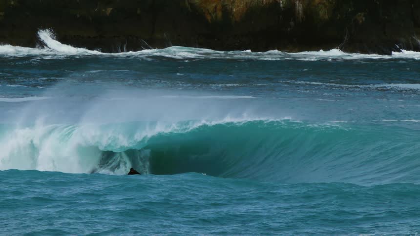 Surfer riding a big wave as it splashes and curls over him