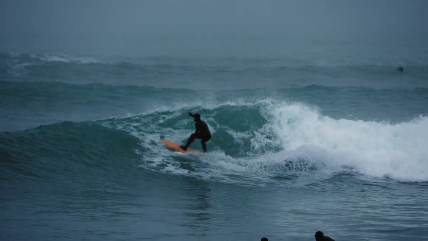 A man is surfing on waves in the ocean while its raining