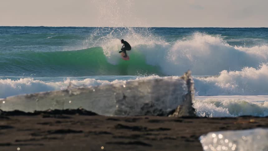 A man surfs the waves near an icecovered coast