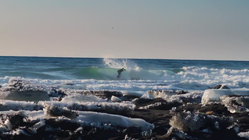 A man surfs the waves near an icecovered coast