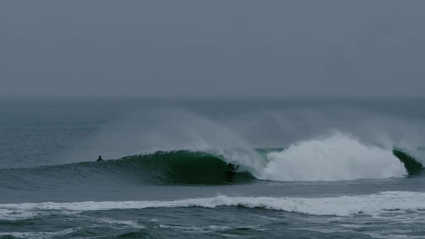 A surfer rides a large wave in the ocean under an overcast sky