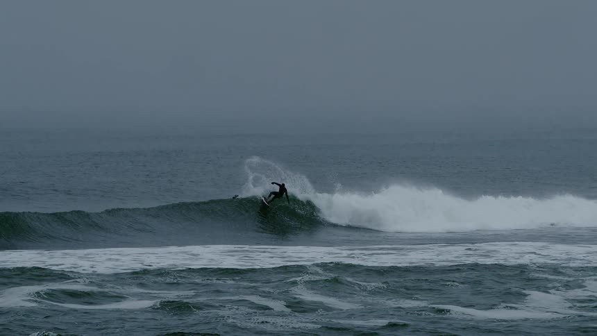 A surfer is riding a large wave on a cloudy day