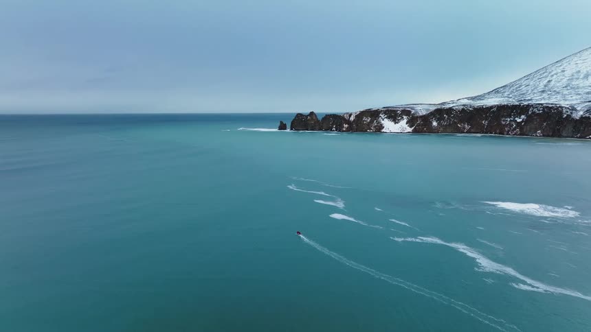 A small boat travels through a vast icy sea with a mountainous coastline in the distance