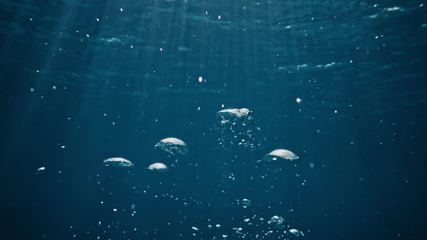 Several clear bubbles rising to the surface under the water of a blue ocean