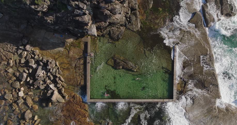 Aerial view of a natural pool sustained by waters that crash against rocks next to the sea