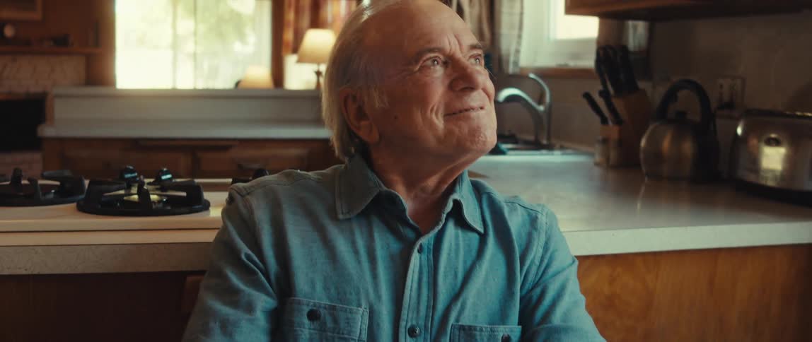 A happy elderly man sitting at the kitchen holding a present
