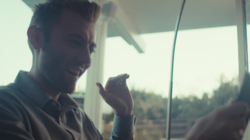 A young man greets someone on a video call using his phone at home